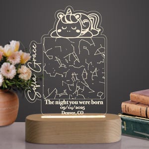 May include: A personalized night light with a sleeping unicorn design. The clear acrylic panel displays a constellation map and the text "The night you were born 09/04/2025 Denver, CO" and the name "Sofia Grace". The base is made of wood.