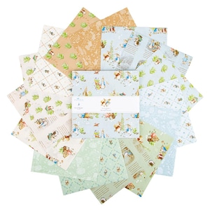 May include: A stack of square fabric swatches arranged in a fan pattern, featuring Peter Rabbit illustrations in shades of blue, green, and tan. A white paper band wraps around the center, printed with the text Peter Rabbit and Riley Blake.