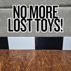 Könnte beinhalten: Das Bild zeigt den Text "NO MORE LOST TOYS!" in fetten weißen Buchstaben vor einem grauen Hintergrund. Darunter befindet sich ein schwarz-weiß gestreifter Rand. Unten ist ein Holzboden zu sehen.