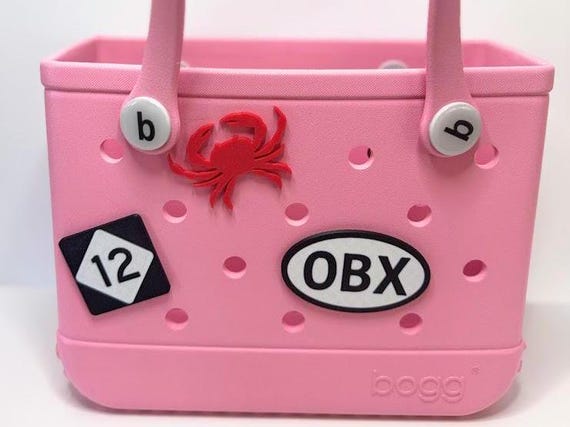 3D printed OBX Outer Banks Bogg Bag charm in ocean blue, flatlay on sand