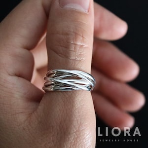 May include: A silver ring with a woven design. The ring is made of multiple strands of silver that are intertwined to create a textured, eye-catching piece of jewelry. The ring is shown on a finger.