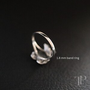 May include: A silver ring with a delicate design, featuring a band that is 1.8 mm wide. The ring is set against a dark background, highlighting its polished finish and intricate details.