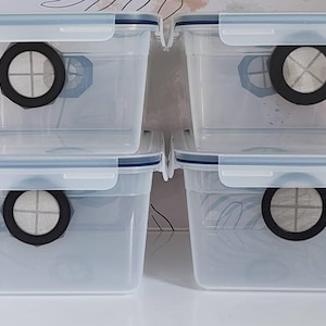 May include: Four rectangular clear plastic storage containers with locking lids. Each container features a circular black-rimmed filter vent on the front side, designed for airflow, with a white mesh screen visible inside the circular opening.