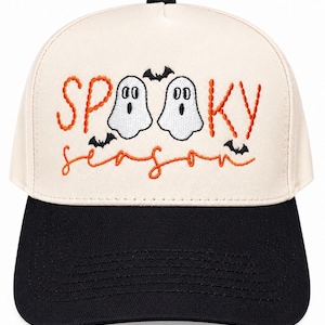 May include: A cream-coloured baseball cap with a black brim featuring embroidered text that reads SPOOKY in orange, two white ghost figures, and the word season in orange cursive script, accented by three small black embroidered bats.