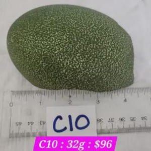 Op de afbeelding: Een groen, getextureerd, ovaalvormig object met een liniaal op de achtergrond. Het object is ongeveer 10 cm lang. Een wit label met de tekst "C10" en het gewicht "32g" is zichtbaar.