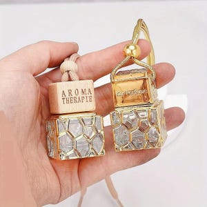 May include: Two gold car air fresheners with a honeycomb design. One air freshener has a wooden tag that says "Aroma Therapie".