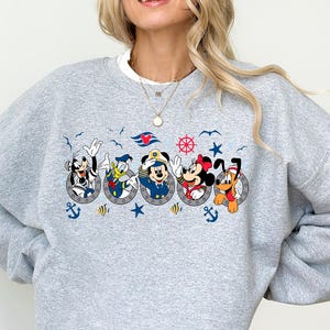 以下が含まれることがあります： ミッキーマウス、ドナルドダック、キャプテンミッキー、ミニーマウス、プルートの海をテーマにしたグラフィックが特徴のグレーのクルーネックのスウェットシャツ。デザインには、錨、星、船の舵が含まれています。スウェットシャツは長袖で、ゆったりとしたフィット感です。