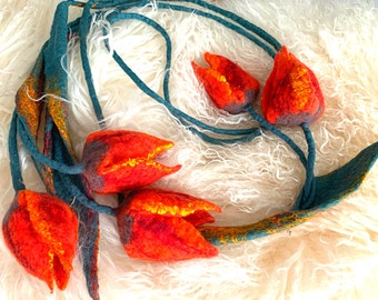 May include: A garland of felt tulips in shades of orange and red with teal green stems. The garland is displayed on a white fluffy surface.