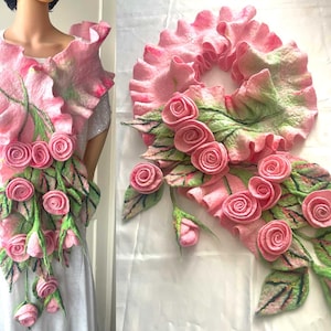 May include: A pink felted floral scarf with a ruffled collar and cascading rose and leaf details. The scarf features multiple pink roses and green leaves, creating a three-dimensional effect. The design is displayed on a mannequin.