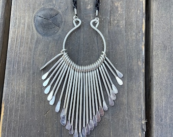 May include: A silver necklace with a large, open circle pendant and a fringe of silver spikes. The necklace is on a black cord.