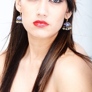 May include: A woman with long dark brown hair wearing a red strapless top and blue and gold earrings.