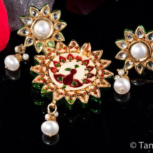 May include: A set of three gold-tone earrings with white pearls and green and red enamel accents. The center earring features a peacock design.