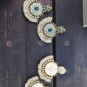 May include: Four pairs of gold earrings with pearl accents. Each earring features a round, decorative center piece with green and white enamel designs.