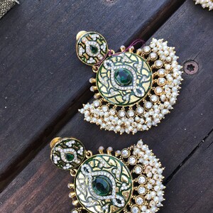 May include: A pair of gold earrings with green and white enamel and pearl accents. The earrings feature a round design with a green stone in the center.