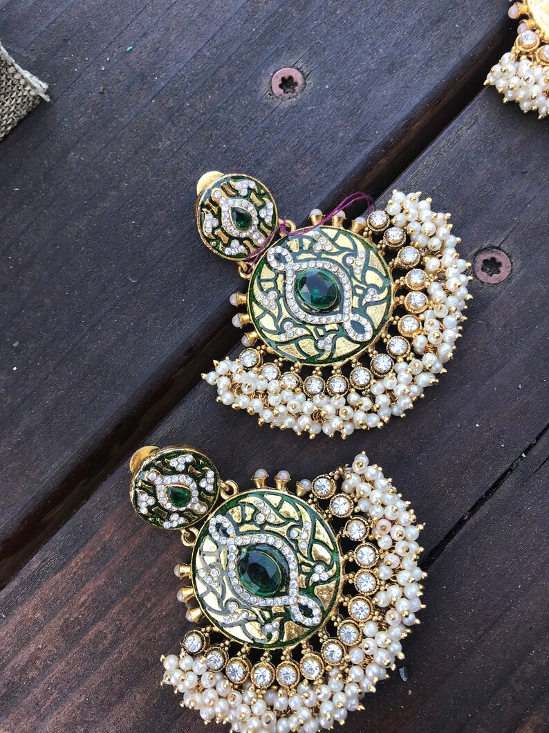 May include: A pair of gold earrings with green and white enamel and pearl accents. The earrings feature a round design with a green stone in the center.