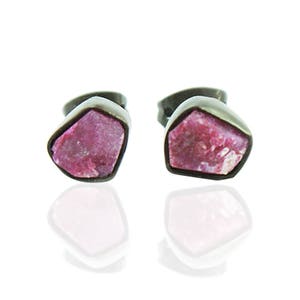 May include: A pair of silver stud earrings with pink ruby gemstones. The earrings are set in a simple, modern style.