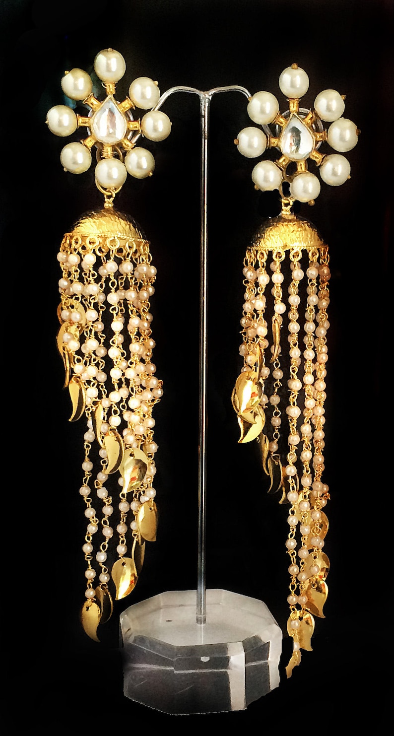 May include: A pair of gold earrings with pearl and crystal accents. The earrings feature a dangling design with multiple layers of gold chains and leaf-shaped charms.