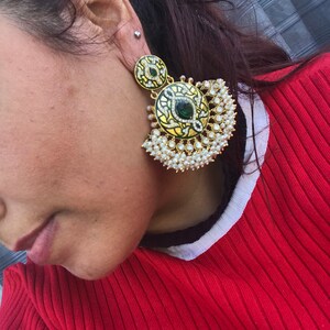 May include: A pair of gold earrings with green and white enamel and pearl accents. The earrings are in the shape of a crescent moon with a round pendant.
