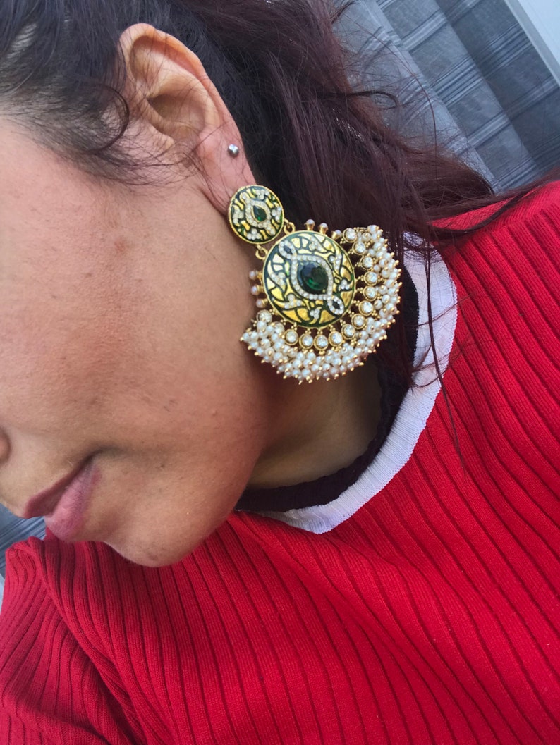 May include: A pair of gold earrings with green and white enamel and pearl accents. The earrings are in the shape of a crescent moon with a round pendant.