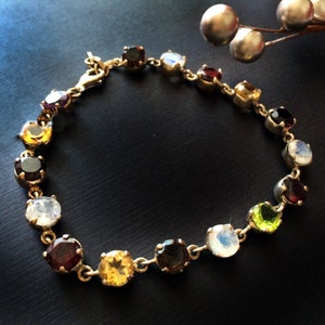 May include: A gold bracelet with a variety of colorful gemstones, including red, green, yellow, and white.
