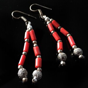 May include: A pair of dangle earrings with red coral beads and silver accents. The earrings have a simple hook closure.