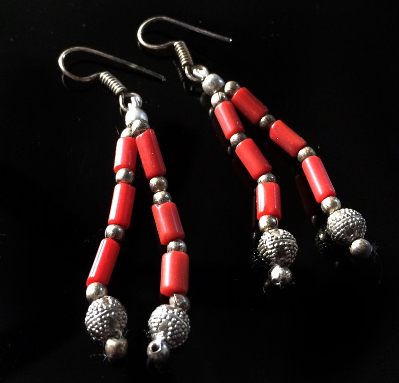 May include: A pair of dangle earrings with red coral beads and silver accents. The earrings have a simple hook closure.