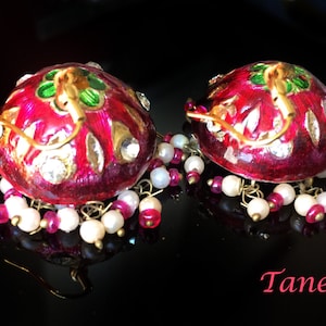 May include: A pair of red and gold earrings with white and pink beads. The earrings are decorated with intricate floral designs and have a traditional Indian style.