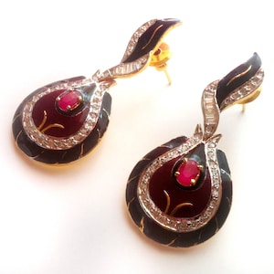 Puede incluir: Un par de pendientes de oro con esmalte negro y una piedra preciosa roja. Los pendientes tienen forma de lágrima y un diseño de diamantes.