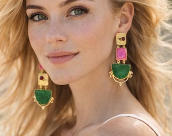 May include: Gold-toned earrings with pink, green, and red accents. The earrings have a rectangular top, a square middle, and a curved bottom. The green section has a textured appearance. The woman in the image is wearing a white top.