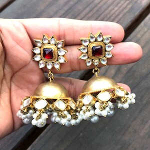 May include: Gold earrings with a red stone center and white pearl accents.