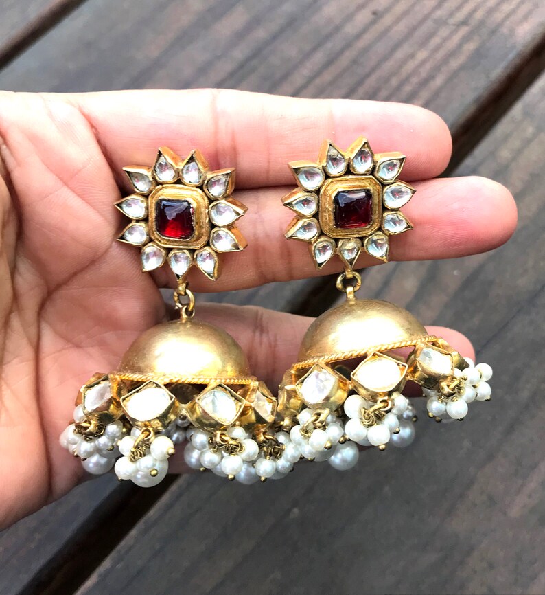 May include: Gold earrings with a red stone center and white pearl accents.
