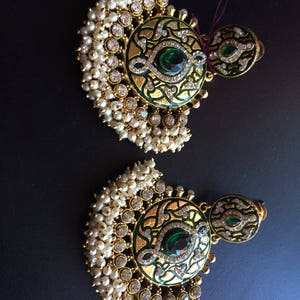May include: A pair of gold earrings with green and white enamel designs. The earrings are adorned with white pearls and clear rhinestones.