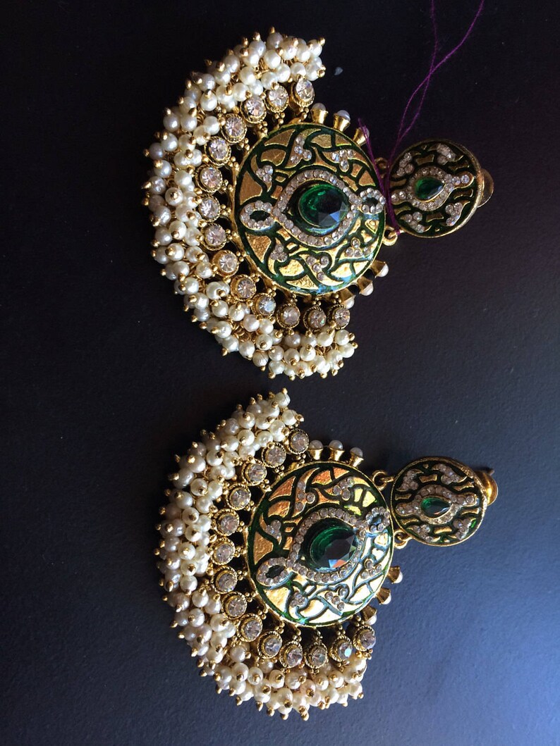 May include: A pair of gold earrings with green and white enamel designs. The earrings are adorned with white pearls and clear rhinestones.