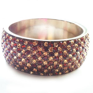 May include: A silver bangle bracelet with a wide band of brown and gold rhinestones.