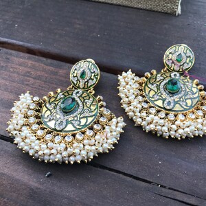 May include: A pair of gold earrings with green and white enamel and pearl accents. The earrings are in the shape of a crescent moon with a round, ornate design in the center.