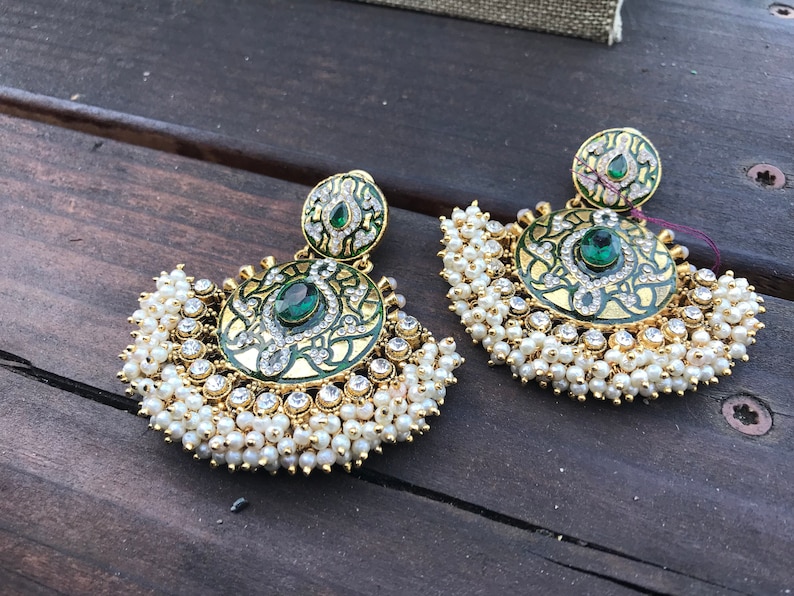 May include: A pair of gold earrings with green and white enamel and pearl accents. The earrings are in the shape of a crescent moon with a round, ornate design in the center.
