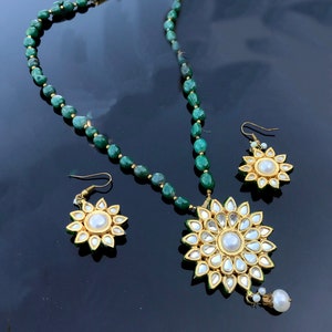 May include: A green gemstone beaded necklace with a large gold pendant featuring a white pearl surrounded by smaller white stones. Matching earrings with a white pearl center and smaller white stones.