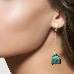 Puede incluir: Pendientes de aro dorados con un colgante de piedra preciosa verde. La piedra preciosa tiene una forma irregular y tosca.