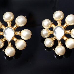 May include: A pair of gold earrings with a clear gemstone in the center and surrounded by white pearls.