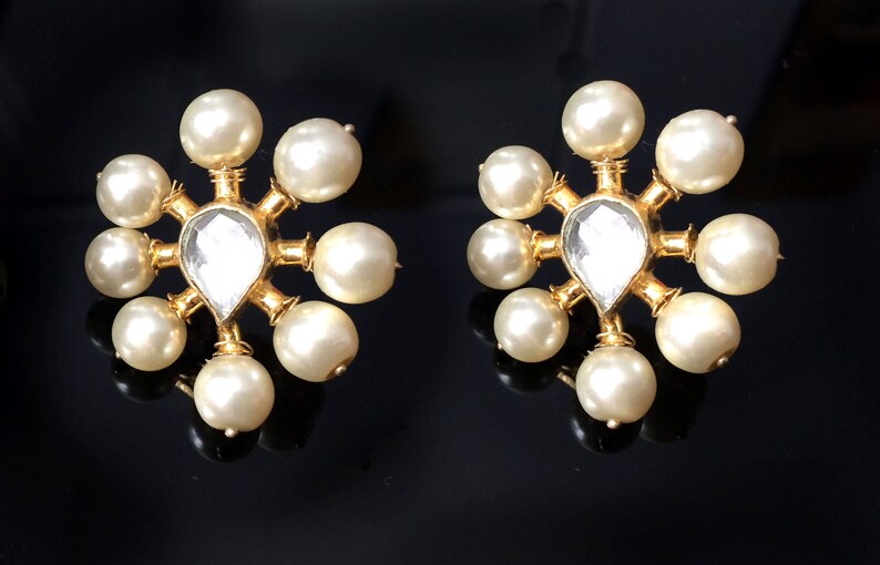 May include: A pair of gold earrings with a clear gemstone in the center and surrounded by white pearls.