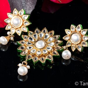 May include: A set of three gold-tone earrings with green enamel and white pearl accents. The earrings are shaped like flowers with multiple layers of petals.