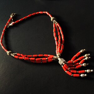 May include: A red coral necklace with silver beads and a tassel. The necklace is made of three strands of coral beads and has a silver clasp.