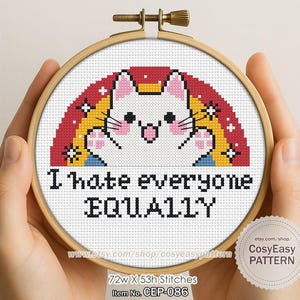 May include: A cross-stitch embroidery hoop with a white cat design, a rainbow, and the text "I hate everyone EQUALLY." The embroidery is in a wooden hoop. The item number is CEP-086.