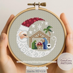 Könnte beinhalten: Eine Kreuzstich-Stickerei in einem Holzrahmen zeigt eine Krippenszene in einer Halbmondform. Das Design zeigt den Weihnachtsmann, einen Stall und ein Schaf, mit Schneeflocken und einer Palme. Der Text "CosyEasy PATTERN" ist sichtbar.