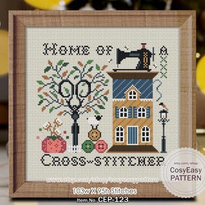 May include: Cross-stitch pattern framed in wood. The design features a house, sewing machine, scissors, and the text "HOME OF CROSS-STITCHER". The color palette includes shades of brown, blue, green, and red. The pattern measures 103w X 95h stitches.