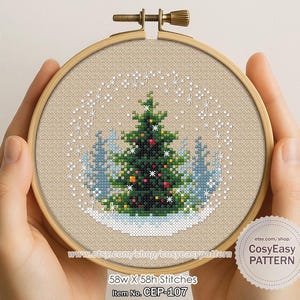 May include: A cross-stitch Christmas tree design in a wooden embroidery hoop. The tree is green with red and yellow ornaments, set against a snowy landscape. The design is 58 stitches wide and high. The text "CosyEasy PATTERN" is visible.