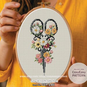 May include: Cross-stitch design featuring scissors filled with flowers, presented in an embroidery hoop. The floral arrangement includes daisies and roses. The text reads "52w X 107h Stitches" and "Item No. CEP-146". The hoop measures approximately 132cm x 272cm.