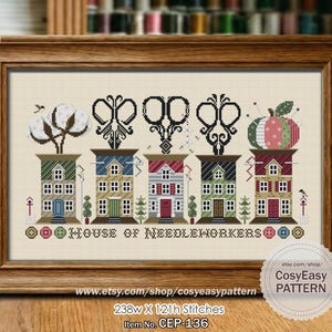 May include: A framed cross-stitch design depicting five houses, each with a different sewing-related motif, such as scissors and a cotton plant. The words "HOUSE OF NEEDLEWORKERS" are stitched below. The pattern is presented in a wooden frame.