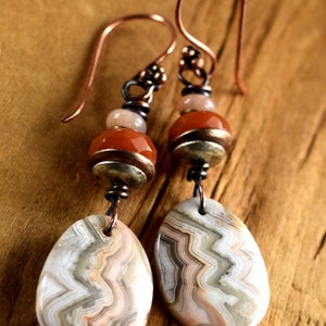 May include: A pair of copper earrings with agate stone drops. The earrings feature copper wire wrapped around orange and white beads.