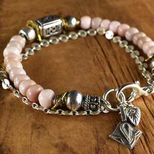 May include: A pink opal beaded bracelet with silver and gold accents. The bracelet has a lobster clasp closure and two charm pendants.